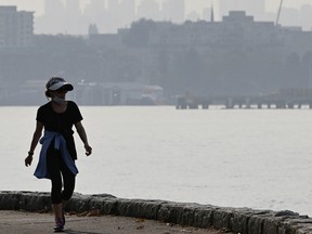 A pedestrian walks along the seawall in Vancouver as smoke shrouds the skyline.