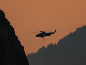 A helicopter with a water bucket battling the Flood Falls Trail wildfire picks up water from the Fraser River, in Hope, B.C., Monday, Sept. 12, 2022. Cool, showery weather is helping wildfire crews make progress on the five highly visible or potentially damaging wildfires currently burning in British Columbia.