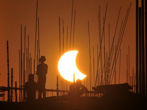 Labourers work at a construction site as the moon partially obscures the sun during a partial solar eclipse visible from Gurgaon on October 25, 2022.