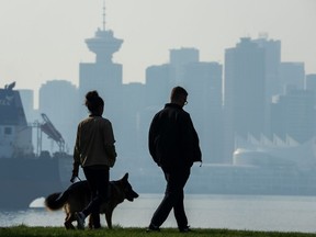 People walk a dog in Vancouver, Tuesday, October 18, 2022. Nine record high temperatures for the date have been set across British Columbia, but Environment Canada says the unseasonable heat is ending and rain or snow will arrive in some areas as early as Friday.