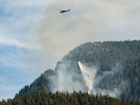 A helicopter dumps water on a forest fire in West Vancouver on Friday, Oct. 14, 2022.