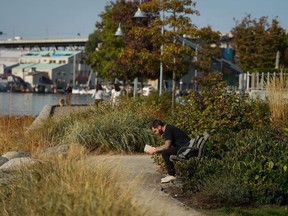 A man reads a book while sitting on a bench on the False Creek seawall in Vancouver, B.C., Thursday, Oct. 13, 2022.