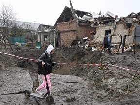 A girl carries a kick scooter as she walks past a crater after a missile strike in a village, near the western Ukrainian city of Lviv, on November 16, 2022, amid the Russian invasion of Ukraine.