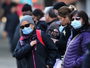 Masked commuters wait for their bus in downtown Vancouver on Monday.