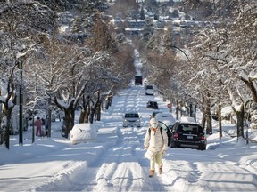 A woman bundled up for the cold weather walks up a snow-covered street after 21 centimetres of snow fell overnight, in Vancouver, on Thursday, December 30, 2021.