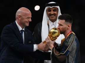 Argentina's captain Lionel Messi kisses the World Cup trophy as FIFA President Gianni Infantino and Qatar's Emir Sheikh Tamim bin Hamad al-Thani look on.