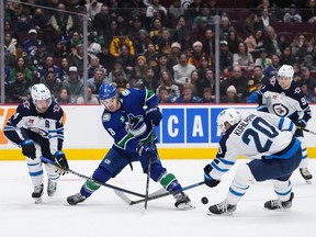 Vancouver Canucks' Conor Garland (8) loses the puck as he tries to skate past Winnipeg Jets' Josh Morrissey (44) and Karson Kuhlman (20) during the first period of an NHL hockey game in Vancouver, on Saturday, December 17, 2022.