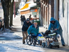 A passer-by (left) helps two men with wheelchairs navigate the icy sidewalks along Gore Avenue in Vancouver.