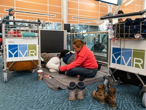 Rowendel Cabager passes the time on her phone while her husband Dale and daughter Shykiel Clair try to sleep while they wait at Vancouver International Airport for a flight to Calgary on Dec. 23, 2022.