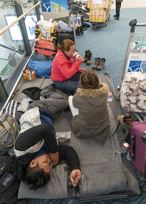 Rowendel Cabager (top) and daughter Shykiel Clair sit and talk while her husband Dale tries to sleep as they wait at Vancouver International Airport for a flight to Calgary on Dec. 23, 2022.