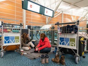 Rowendel Cabager (right) and daughter Shykiel Clair sit while her husband Dale tries to sleep as they wait at Vancouver International Airport for a flight to Calgary on Dec. 23, 2022.