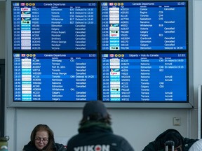 Delays and cancelled flights fill the departures board screens at Vancouver International Airport as passengers find any available space to pass the time on Dec. 23, 2022.
