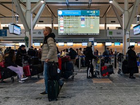 Eager travellers line up in various lines hoping to check in for their flights at Vancouver International Airport as delays and cancelled flights fill the departures board on Dec. 23, 2022.