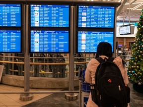 A woman stares at a departures board at Vancouver International Airport as delays and cancelled flights fill the screens on Dec. 23, 2022.
