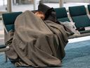 A woman gets some sleep in a pair of seats in the Vancouver International Airport terminal as delays and canceled flights abound due to snow on December 23, 2022.
