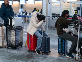 A woman gets some shut eye while waiting in line to check in for her flight at Vancouver International Airport, as weather delays and cancelled flights caused by winter weather take hold on Dec. 23, 2022.
