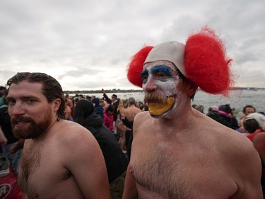 A person dressed as a clown and others walk back onto the beach after plunging into English Bay during the Polar Bear Swim, in Vancouver, B.C., Sunday, Jan. 1, 2023.