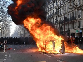 French riot police stand behind a car in fire on the sidelines of a demonstration on the fourth day of nationwide rallies in Paris on February 11, 2023.