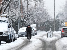 a cyclist makes their way down a snowy vancouver street.