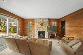 The family room inside 973 Lombardy Drive in Port Coquitlam showcases wood-accent walls, floor-to-ceiling stone-surround wood-burning fireplace and a wet bar.
