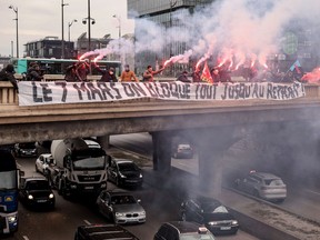 Bus drivers of state-owned RATP, which operates the greater Paris transport system, burn flares behind a banner reading in French "on March 7, let's block everything until withdrawal" on a bridge above Paris's ring road on March 6, 2023, as massive strikes are expected from March 7 in France against French government's proposed pension reform.
