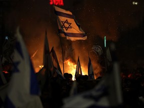 Protesters block a road and hold national flags as they gather around a bonfire during a rally against the Israeli government's judicial reform in Tel Aviv, Israel on March 27, 2023. - Israeli Prime Minister Benjamin Netanyahu on March 26, 2023 fired Defence Minister Yoav Galant a day after he broke ranks, citing security concerns in calling for a pause to the government's controversial judicial reforms. On a day when 200,000 people took to the streets of Tel Aviv to protest the reforms, Galant -- who had been a staunch Netanyahu ally -- on Saturday said "we must stop the legislative process" for a month in view of its divisiveness.