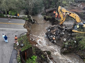 In an aerial view, workers make emergency repairs to a road that was washed out heavy rains on March 10, 2023 in Soquel, Calif.