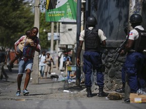 A parent, carrying his child after picking him up from school, runs past police as they carry out an operation against gangs in the Bel-Air area of Port-au-Prince, Haiti, Friday, March 3, 2023.