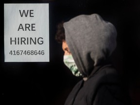 A pedestrian wearing mask in front of a sign advertising hiring in Toronto.