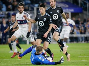 Minnesota United goalkeeper Clint Irwin makes a sliding save as United defenders Miguel Tapias and Brent Kallman make sure Vancouver Whitecaps forward Brian White doesn't get to the ball in the first half of an MLS soccer game Saturday, March 25, 2023, in St. Paul, Minn.