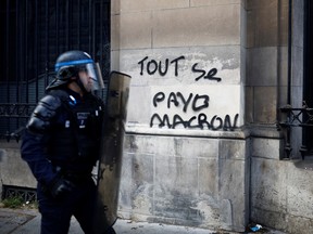 French CRS riot police walks past a slogan reading "Everything has a price, Macron" during a demonstration as part of the 12th day of nationwide strikes and protests against French government's pension reform, in Paris, France, April 13, 2023.  REUTERS/Stephane Mahe