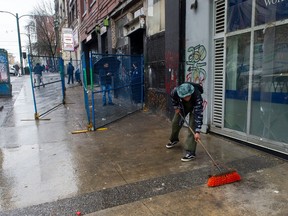 A man sweeps debris from the sidewalk on E. Hastings St. Thursday. City works crews continue for the second day to clear the tent encampment along E. Hastings Street in Vancouver, BC Thursday, April 6, 2023. Tents and belongings are being removed and at the same time the streets and sidewalks are being hosed-down, under the eyes of the VPD and fire officials.  
(Photo by Jason Payne/ PNG)