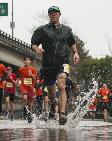 A runner goes through a puddle along Pacific Blvd in the 2023 Sun Run in Vancouver on April 16, 2023.