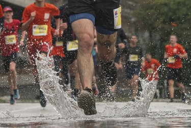 A runner makes a splash through a puddle along Pacific Blvd in the 2023 Sun Run in Vancouver on April 16, 2023.