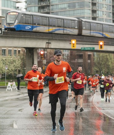 A skytrain passes overhead of Will Matthews and the pack of runners along Quebec Street and Pacific Blvd. in the 2023 Sun Run in Vancouver on April, 16, 2023.