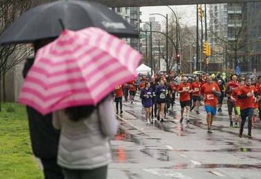 Run supporters huddle under umbrellas to watch runners run along Quebec Street in the 2023 Sun Run in Vancouver on April 16, 2023.
