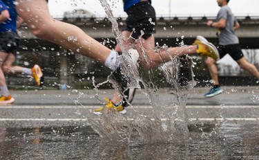 Runners run through a puddle while making their way towards the finish of the 2023 Sun Run in Vancouver on April, 16, 2023.