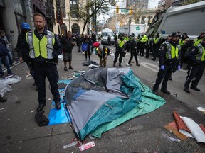Vancouver police officers surround a tent with a person still inside as city workers clear an encampment on East Hastings Street in the Downtown Eastside of Vancouver, B.C., Wednesday, April 5, 2023.