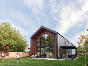 A gabled roof and metal siding evoke the form of a barn, while a two-storey window mimics the shape, reflecting treetops surrounding the large backyard.