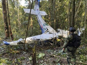 In this photo released by Colombia's Armed Forces Press Office, a soldier stands in front of the wreckage of a Cessna C206, Thursday, May 18, 2023.