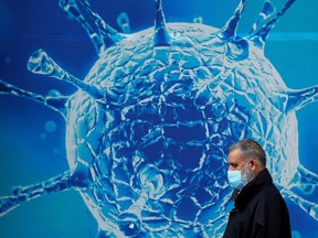 A man wearing a protective face mask walks past an illustration of a virus in Britain.