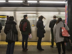 Commuters stand on the platform as an L train passes, New York, U.S.