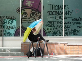 A woman sits under an umbrella outside the Yaletown's Thomus Donaghy Overdose Prevention Site on Friday, May 19, 2023. Wall Financial Group is suing the City of Vancouver over the site on Seymour Street that is next door to condos.