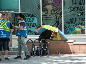 Una mujer sentada bajo un paraguas con una pipa de crack en las manos frente al sitio de prevención de sobredosis Thomas Donaghy de Yaletown el viernes 19 de mayo de 2023.