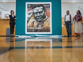 A Canada Post stamp depicting First Nations leader George Manuel is unveiled in North Vancouver, B.C., on Monday, June 12, 2023, by Susan Margles, left, Chief People and Safety Officer at Canada Post, George Manuel Jr., and Doreen Manuel, both children of George Manuel.