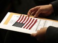 FILE - Abdullah Omar, from Iraq, holds his information packet and an American flag during a naturalization ceremony on Jan. 17, 2020, in Cleveland. Two decades after the U.S. invasion of Iraq, thousands of Iraqis are still trying to emigrate to the United States. An estimated 164,000 Iraqis have already found homes in America since the 2003 invasion. But many are still waiting.