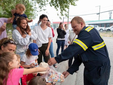 A firefighter distributes candy as West Kelowna, Canada, residents cheer and applaud firefighters returning to their fire hall after battling the McDougall Creek wildfire, on August 21, 2023.