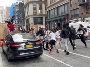 In this photo taken from video, a man jumps on a car as a crowd runs through the street on Broadway near Union Square, Friday, Aug. 4, 2023, in New York.