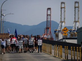 Striking International Longshore and Warehouse Union Canada workers march to a rally as gantry cranes used to load and unload cargo containers from ships sit idle at port in Vancouver on Thursday, July 6, 2023.