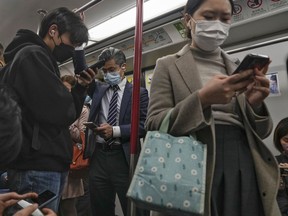 FILE: Commuters wearing face masks browse their smartphones as they ride on a subway train in Hong Kong on Feb. 7, 2023.